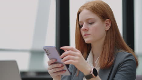 Beautiful-young-business-woman-using-phone-in-office.-Woman-using-a-smartphone-and-leaning-on-a-window-texting-sending-emails-planning-meetings-networking-online-browsing-messages-on-mobile-phone